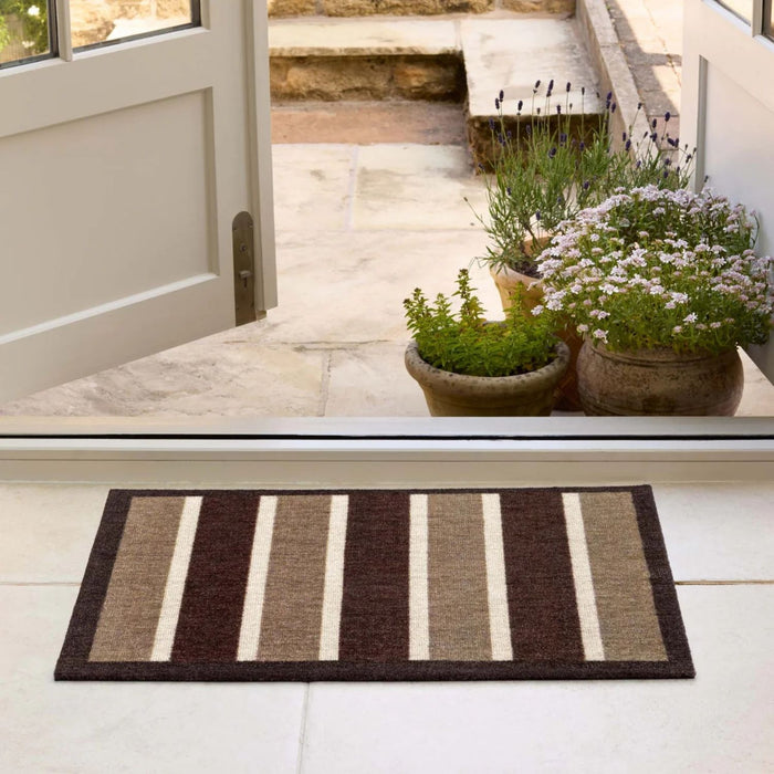 Striped doormat in front of a glass door with plants on a patio