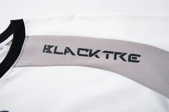 Close-up of a white and gray raglan streetwear tee with black trim and bold KLACTKG graphic on the shoulder