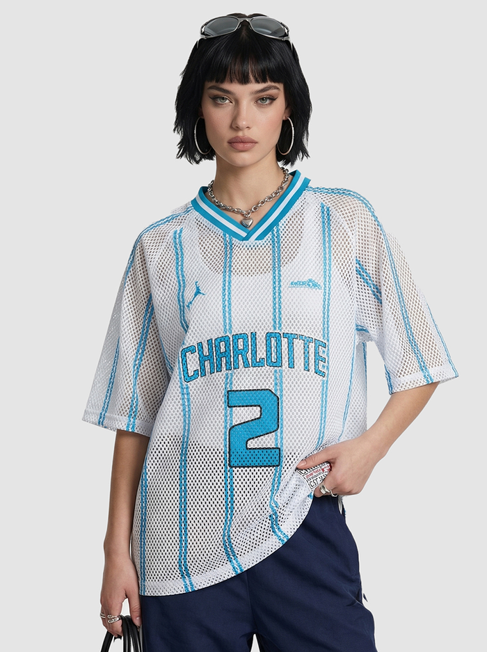Model wearing a white mesh jersey T-shirt with blue stripes, Charlotte 2 graphic, and navy pants on a plain background