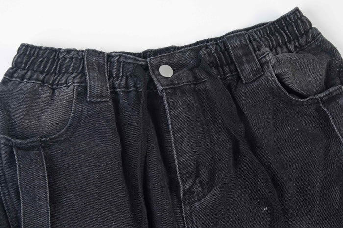 Close-up of black denim waistband with elastic gather, snap button, and belt loop